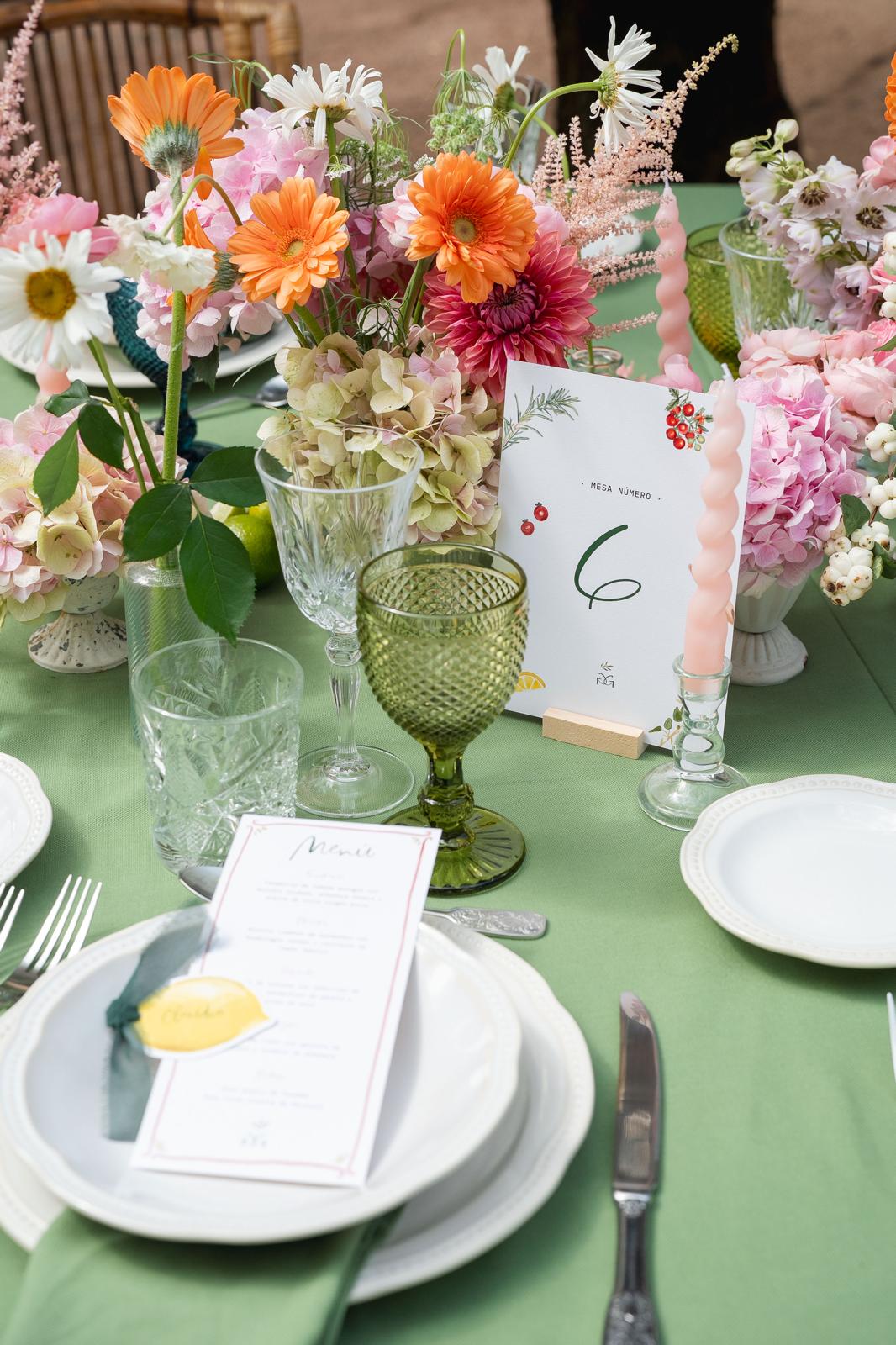 Mesa con mantelería verde, menú y flores de colores