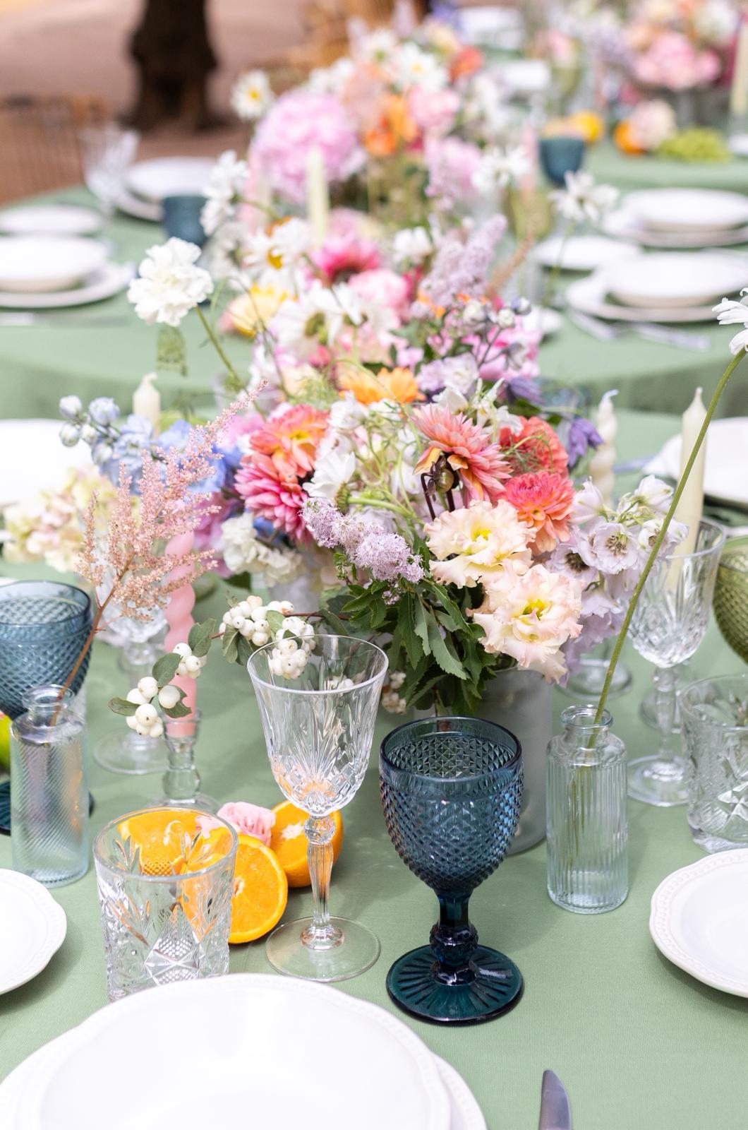 Detalle de mesa con cristalería de color y flores de temporada